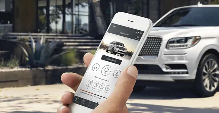 Smartphone avec application de contrôle pour voiture blanche luxueuse en arrière-plan. Technologie automobile.