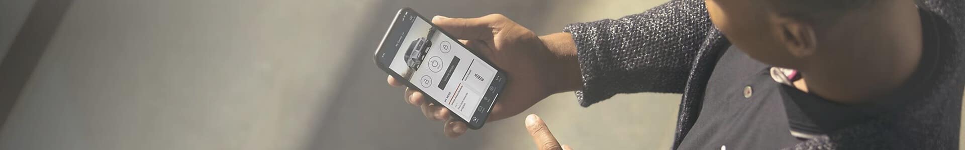 Person holding a smartphone displaying an automotive app with car features and icons.