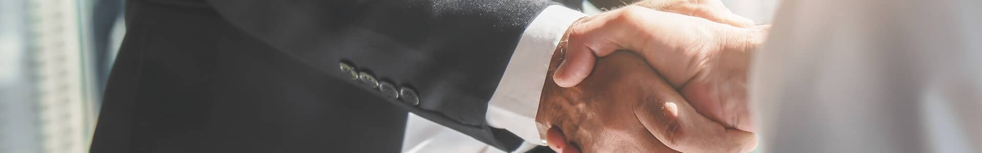 Two people shaking hands, one in a dark suit, symbolizing business partnership.