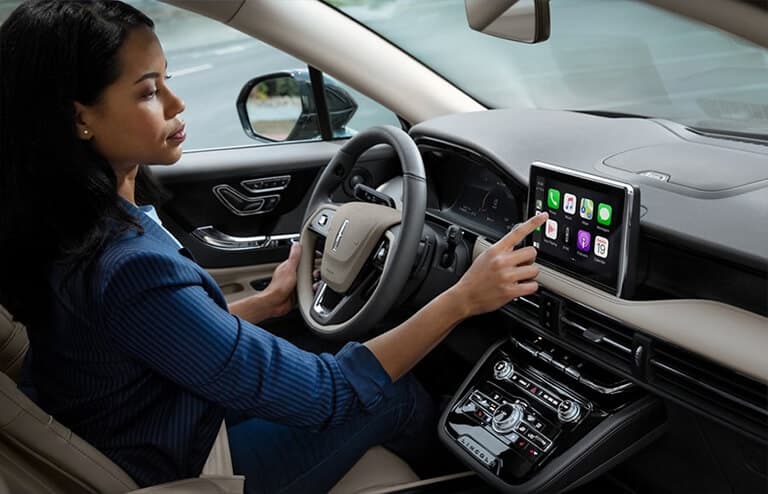 Woman driving a Lincoln vehicle using Apple CarPlay on the dashboard touchscreen