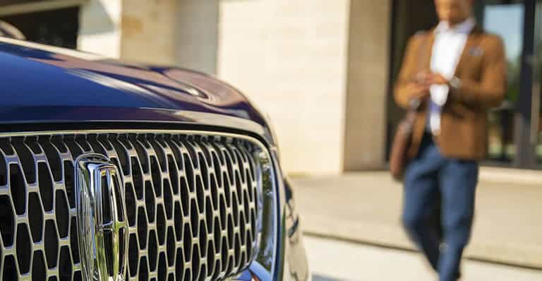 Close-up of a Lincoln vehicle grille with a person walking in the background.