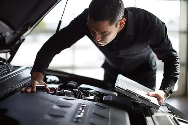 Mechanic inspecting a car engine with a clipboard, ensuring vehicle maintenance.
