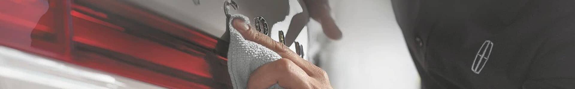 Person polishing a car's rear light with a cloth, wearing a black shirt with a logo.