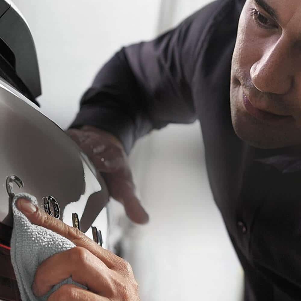 Mechanic adjusting car windshield wiper in a garage, wearing a branded shirt.