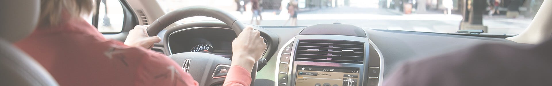 Driver navigating urban street, focusing on the road. Car dashboard and steering wheel visible.