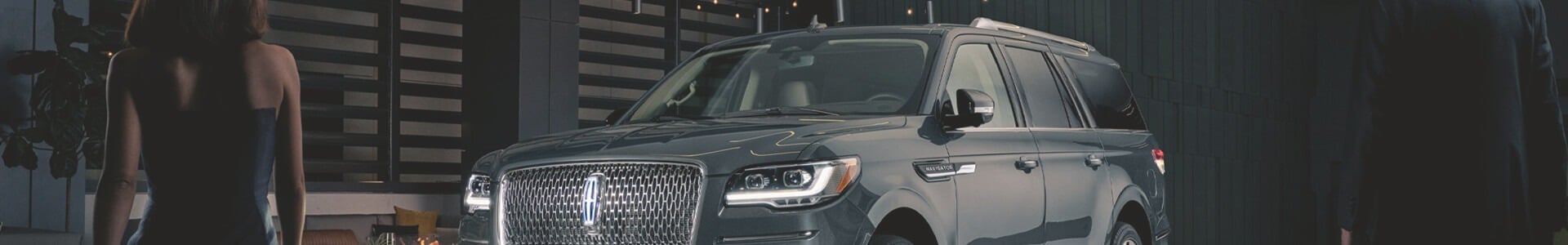 Luxury SUV parked outdoors at night with two people in formal attire nearby.