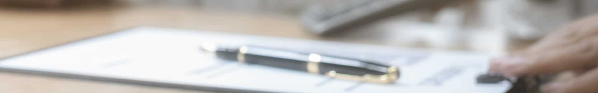 Blurry pen on a document on a wooden desk, suggesting a writing or signing activity.