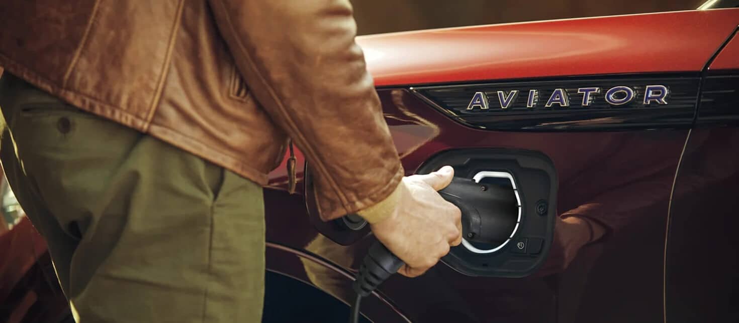 Person plugging in an electric vehicle charger into a red car labeled "Aviator."