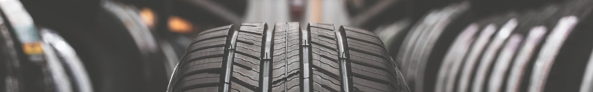 Close-up of a tire with treads, surrounded by blurred rows of tires in a store setting.