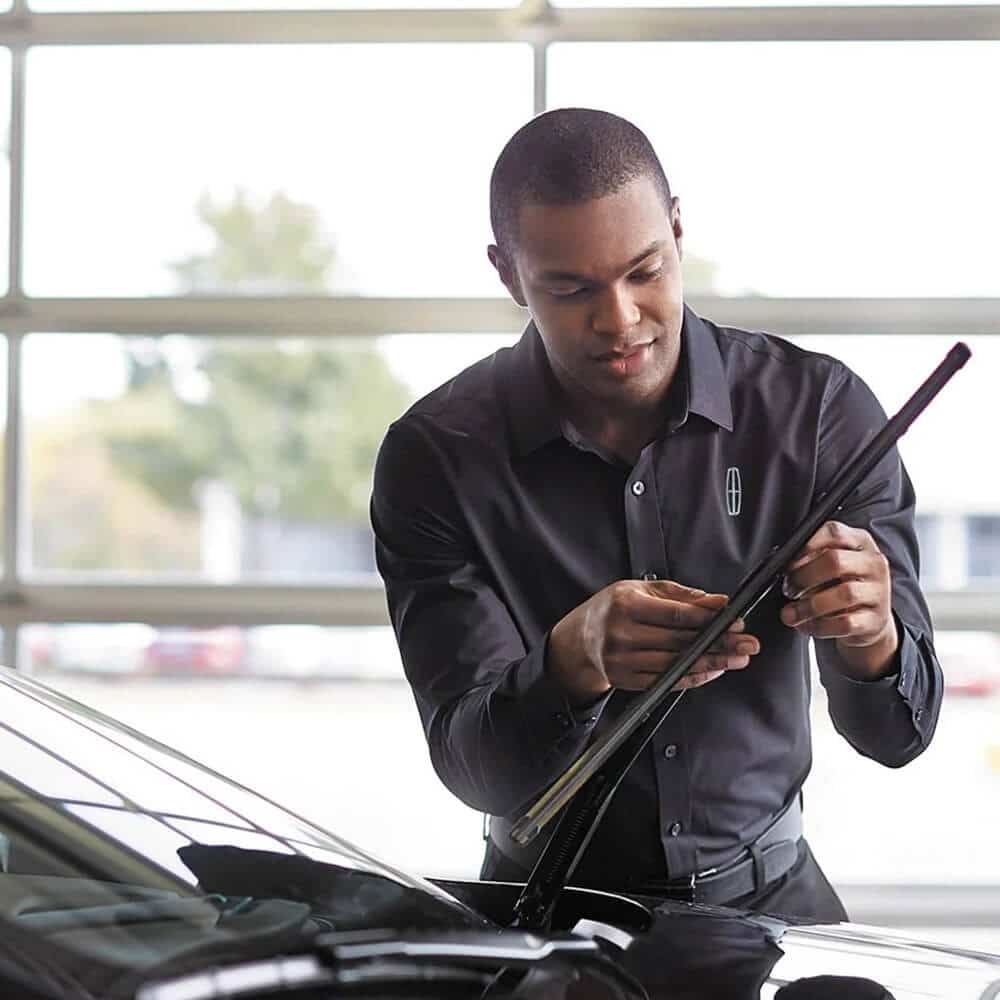 Mechanic adjusting car windshield wiper in a garage, wearing a branded shirt.
