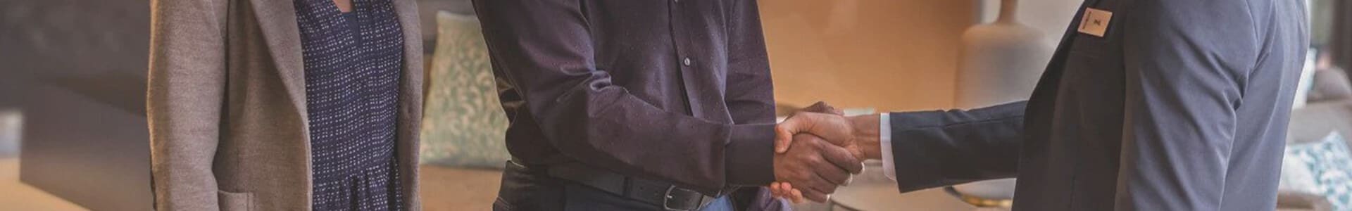 Two people in business attire shaking hands, with a third person standing nearby, indicating a professional agreement.