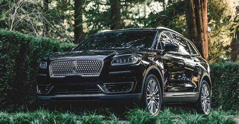 Black Lincoln SUV parked in a lush green setting surrounded by trees.