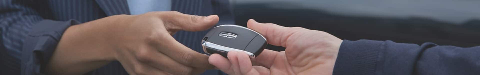 Two hands exchanging a car key fob, symbolizing car ownership or rental.