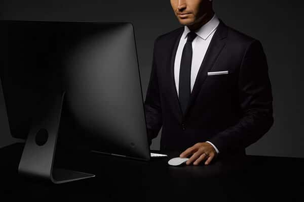Businessman in a suit working on a computer in a dimly lit office setting.