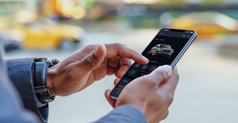 Person using a smartphone app to control car features, with a blurred urban background.