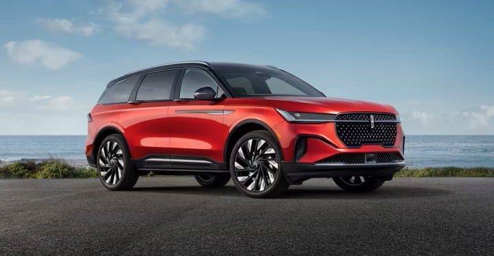 Red SUV parked on a coastal road, ocean in background, showcasing sleek design and modern features.