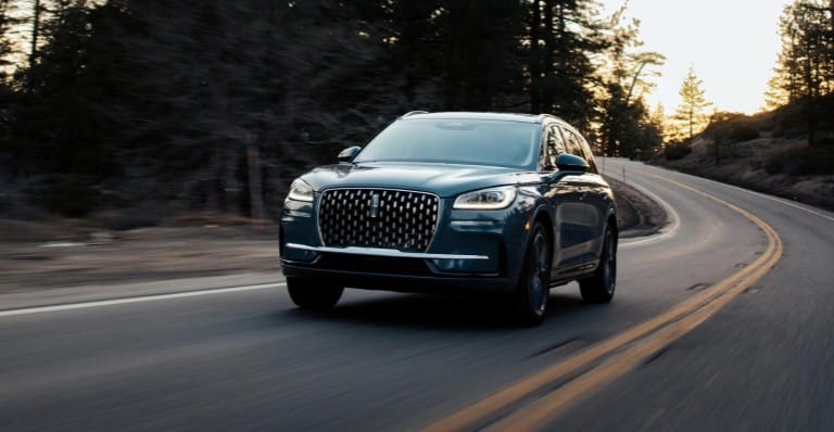 Blue SUV driving on a winding forest road at sunset, highlighting its sleek design.